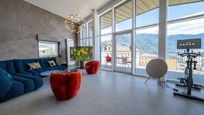 A modern living room with a large window, a blue sofa, red ottomans, and a TV. - Penthouse Annecy74 - Vue panoramique sur le lac (Annecy)