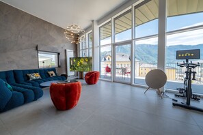 A modern living room with a large window, a blue sofa, red ottomans, and a TV. - Penthouse Annecy74 - Vue panoramique sur le lac (Annecy)