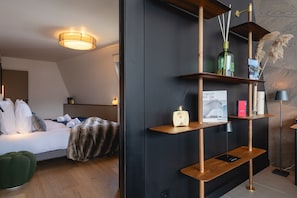 Una habitación de hotel moderna con cama, mesita de noche, estante con adornos y repisa con un cuadro enmarcado.