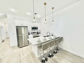 Une cuisine moderne dotée d’appareils électroménagers en acier inoxydable, d’un îlot central blanc avec des tabourets et d’un éclairage suspendu.