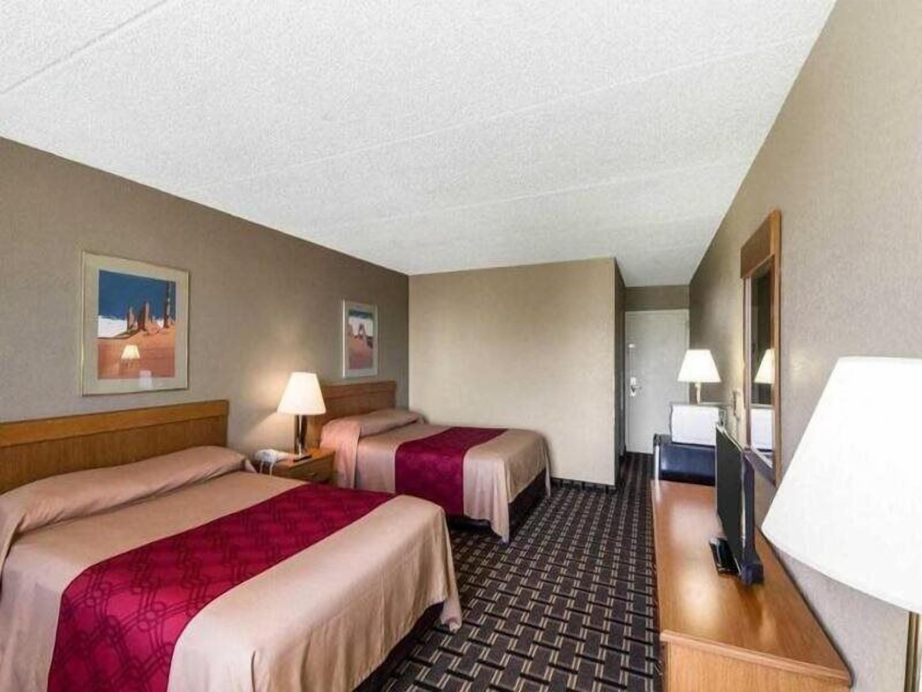 A hotel room with two beds, a desk, a chair, a TV, and a door leading to another room.