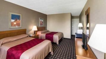 A hotel room with two beds, a desk, a chair, a TV, and a door leading to another room.