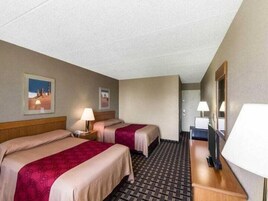 Habitación de hotel con dos camas, un escritorio, una silla, un televisor y una puerta que da a otra habitación.