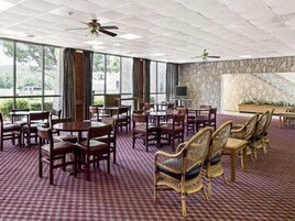Un salón de conferencias de hotel con varias mesas y sillas, ventanas amplias y una pared de acento de piedra.
