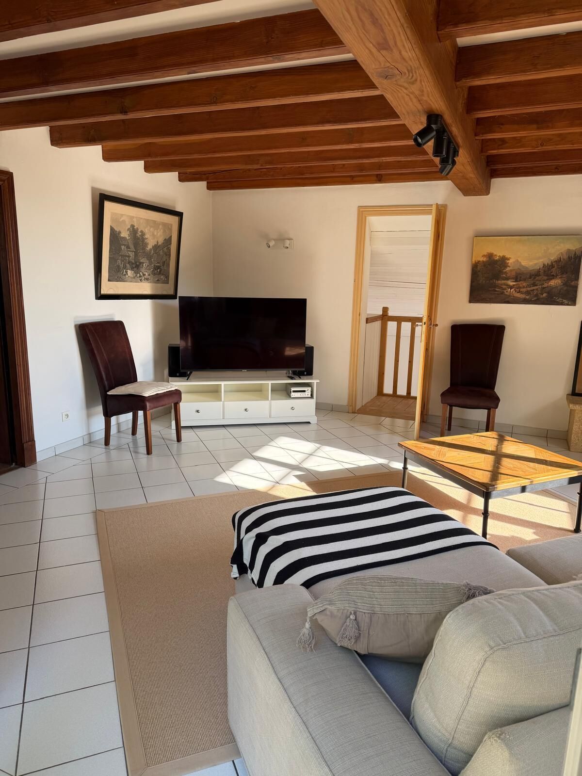 Un salon avec un canapé, des fauteuils, un téléviseur et des œuvres d’art accrochées aux murs.