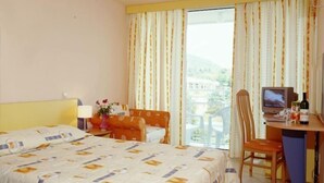 A hotel room with a bed, a desk with a television, a chair, and a window with curtains. - Com (Balchik)