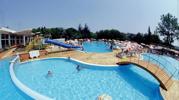 A large outdoor swimming pool with a slide, surrounded by lounge chairs and umbrellas. - Com (Balchik)