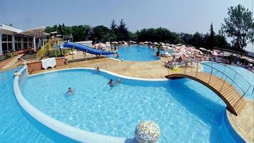 A large outdoor swimming pool with a slide, surrounded by lounge chairs and umbrellas.