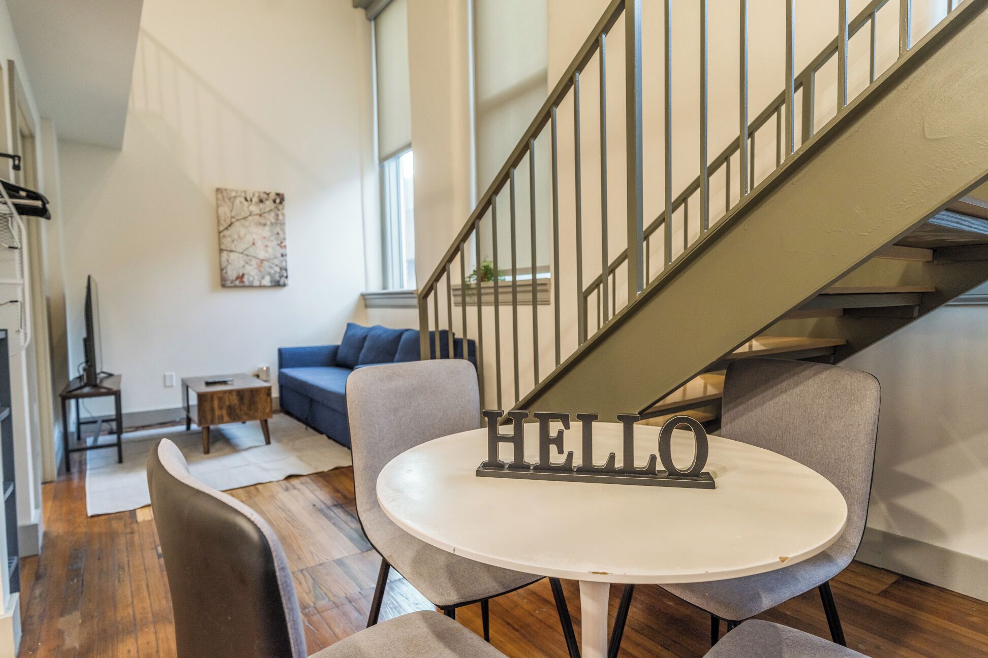 Ein modernes Interieur mit einer Treppe, einem runden Tisch und einem Schild mit der Aufschrift 'HELLO' sowie einem blauen Sofa.