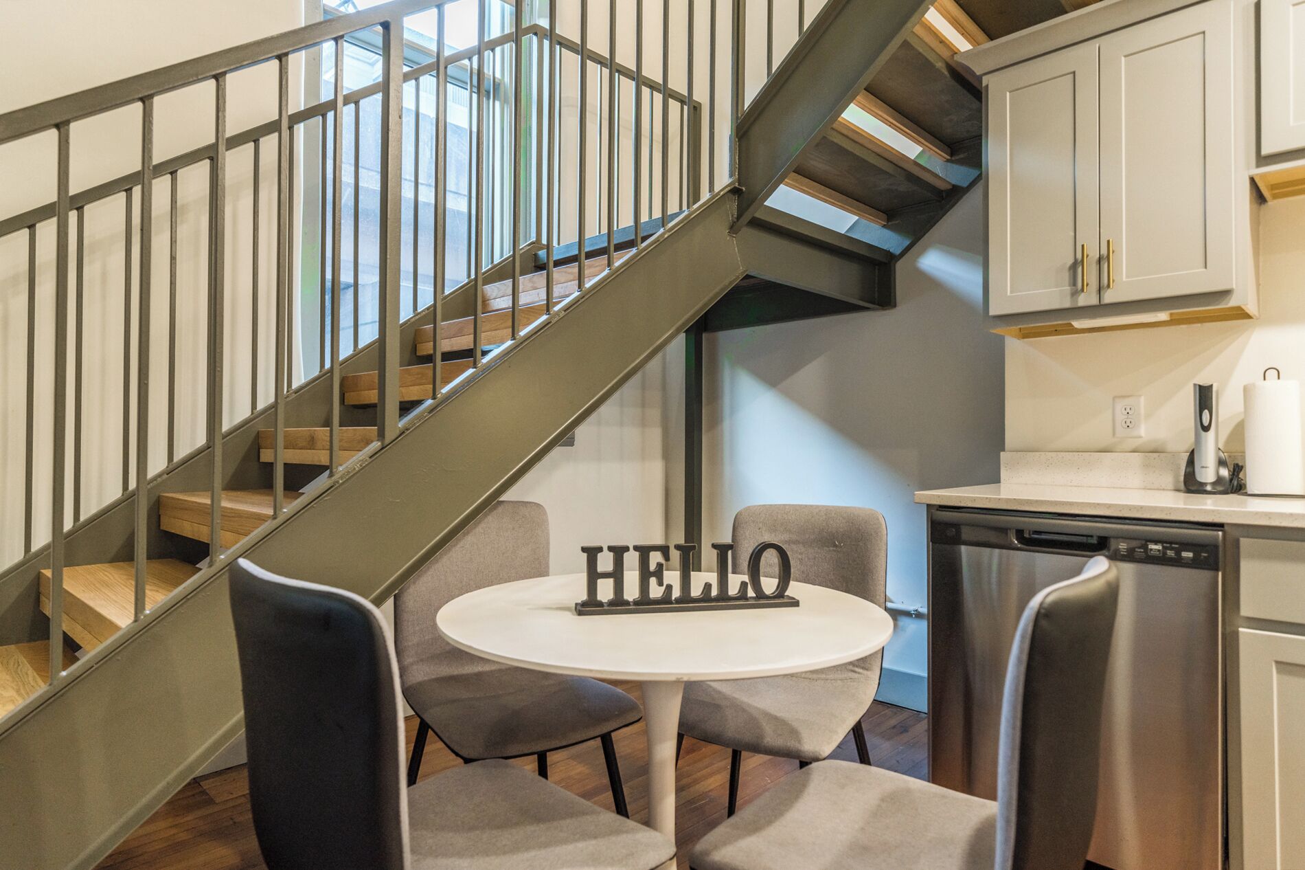 Une cuisine moderne équipée d’un lave-vaisselle intégré, d’une table ronde avec des chaises et d’un escalier doté d’une rampe en métal.