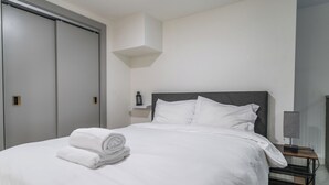 Hotellihuone, jossa on sänky, yöpöytä, lamppu, seinälle kiinnitetty hylly ja vaatekaappi.