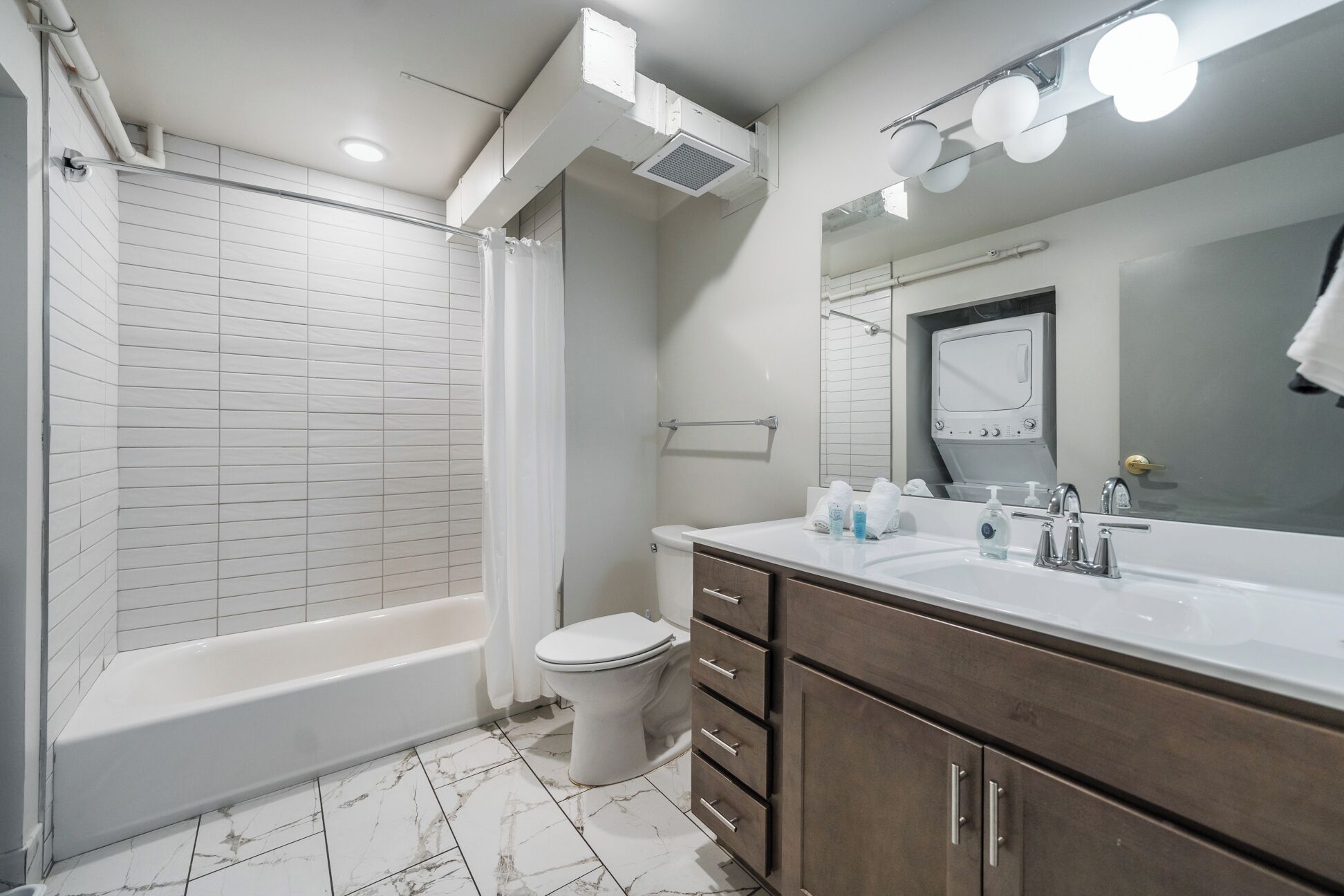 A modern bathroom with a bathtub, toilet, vanity with a mirror, and a shower curtain.