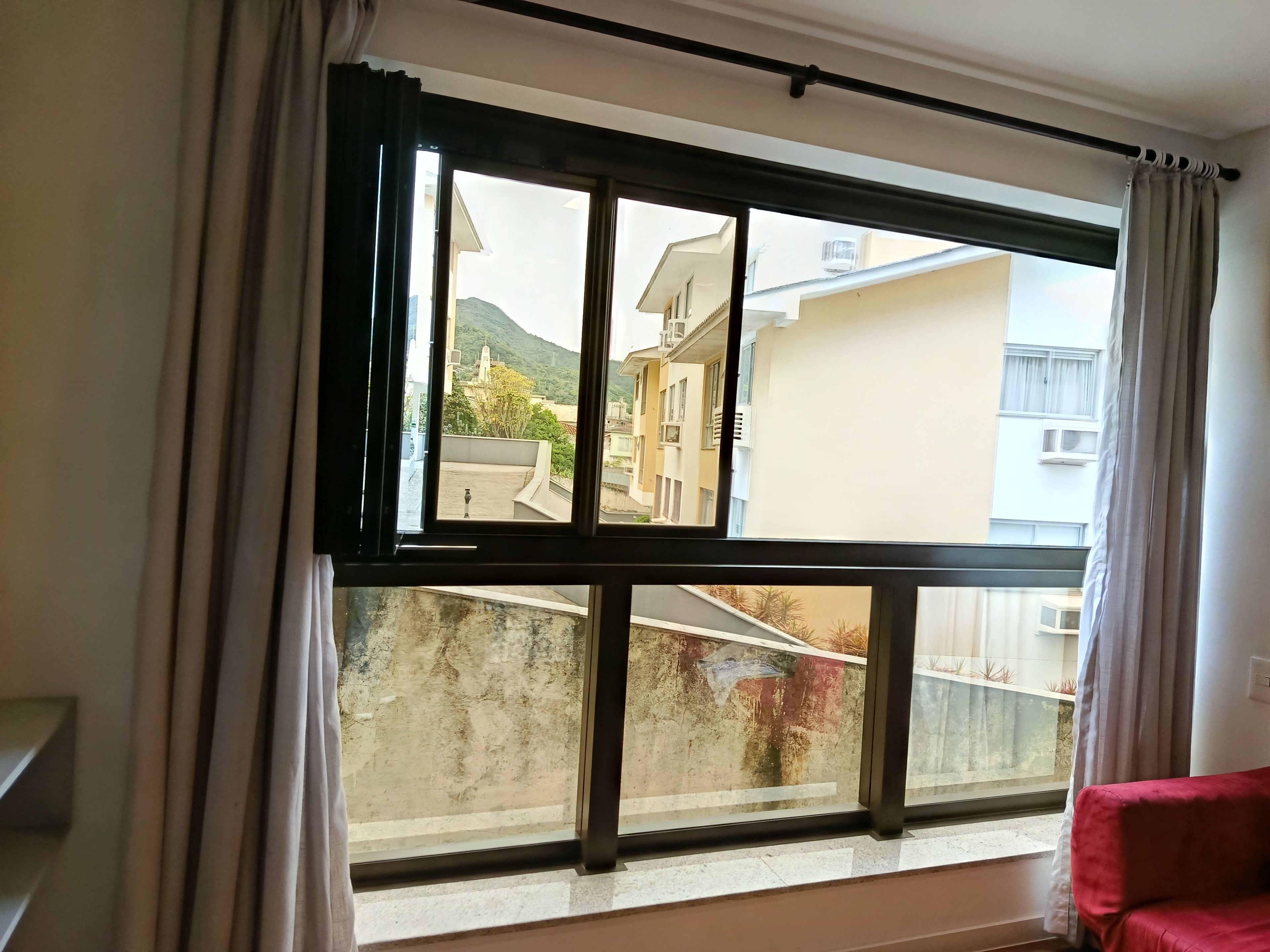 A room with a large window, a red sofa, and a view of buildings and a mountain.
