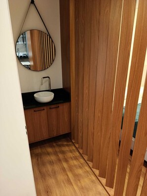 Un baño moderno con tocador de madera, espejo redondo y lavamanos blanco.