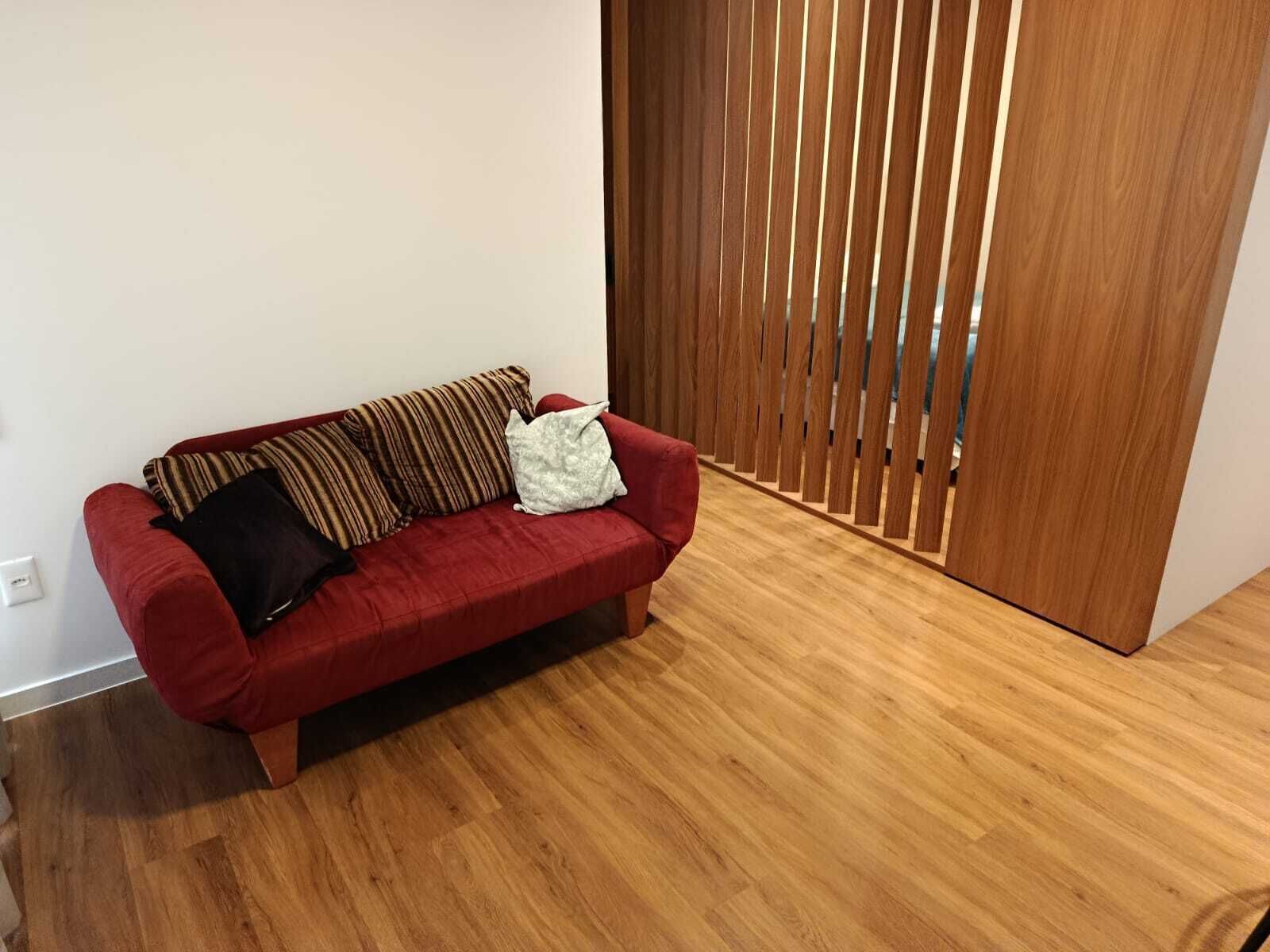 A red sofa with patterned cushions in a room with wooden flooring and a sliding wooden door.