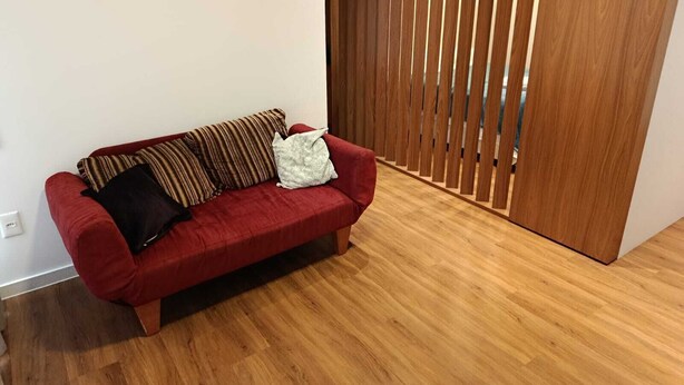 Un divano rosso con cuscini decorati in una stanza con pavimento in legno e una porta scorrevole in legno.