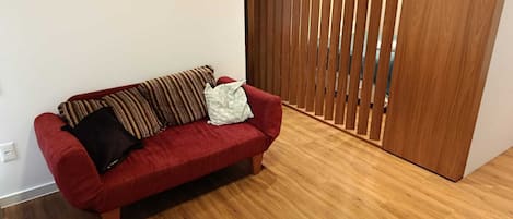 A red sofa with patterned cushions in a room with wooden flooring and a sliding wooden door.