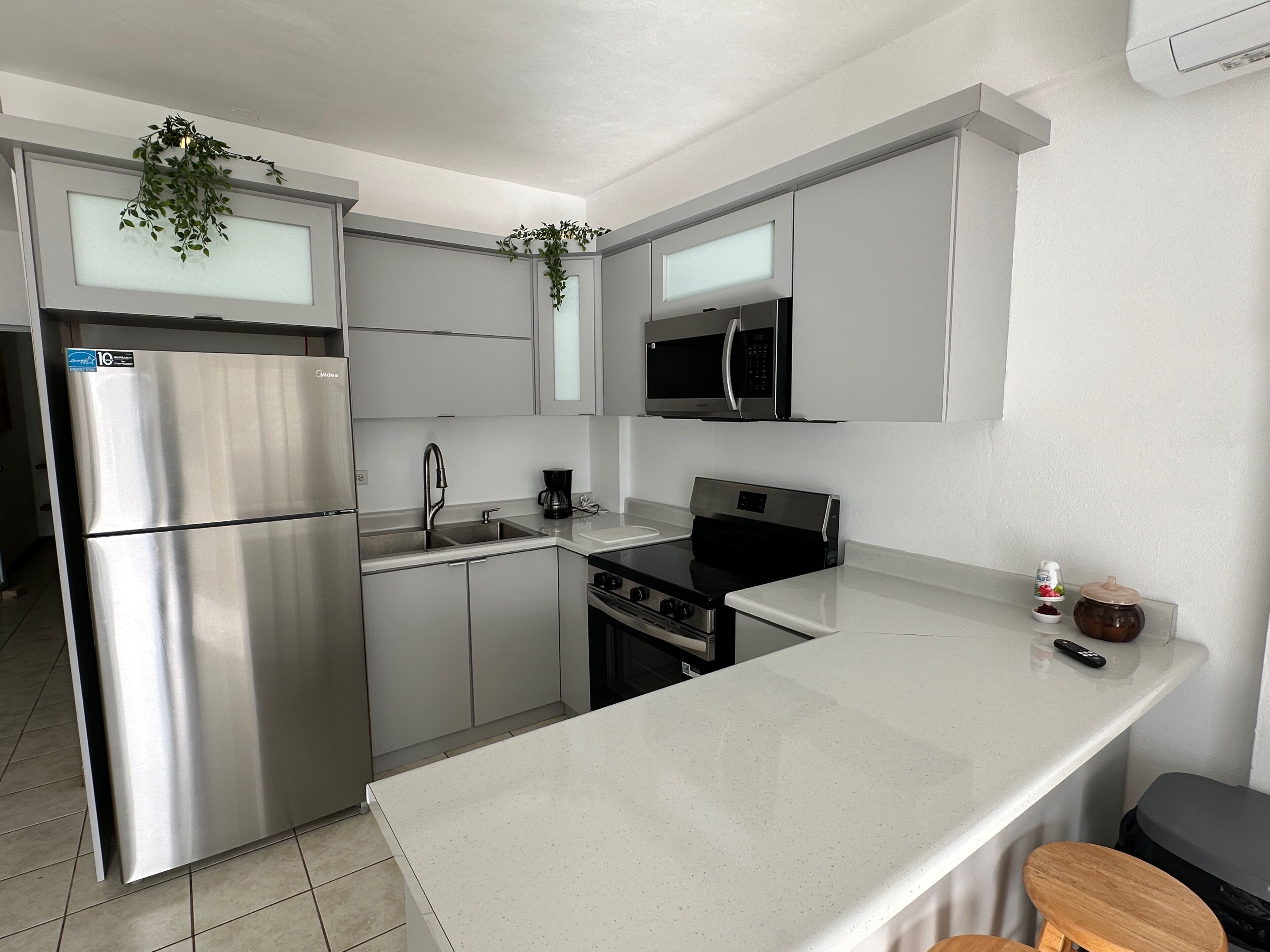 A modern kitchen with stainless steel appliances, a white countertop, and a small stool.