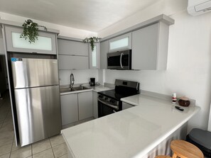 A modern kitchen with stainless steel appliances, a white countertop, and a small stool. - Delightful 2-bedroom apartment with AC in charming Combate (Combate)
