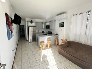Ein kompakter Wohnraum mit Küchenzeile, einem braunen Sofa und einem an der Wand befestigten Fernseher.