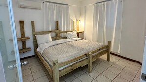 Ein Schlafzimmer mit einem hölzernen Bett, weißen Vorhängen, einer Nachttischlampe und einer Wand-Klimaanlage.