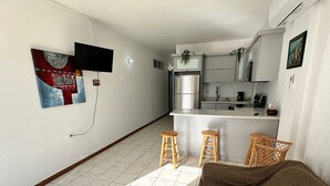 Eine kompakte Küche mit Kochinsel, Barhocker und einem an der Wand befestigten Fernseher.