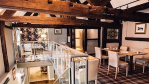 Un restaurant doté d’un sol à carreaux, de poutres en bois et d’une balustrade en verre donnant sur une salle à manger située en contrebas.