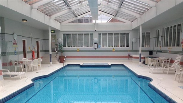 Une piscine intérieure à l’eau d’un bleu cristallin, entourée de chaises longues blanches et dotée d’un mur en verre.