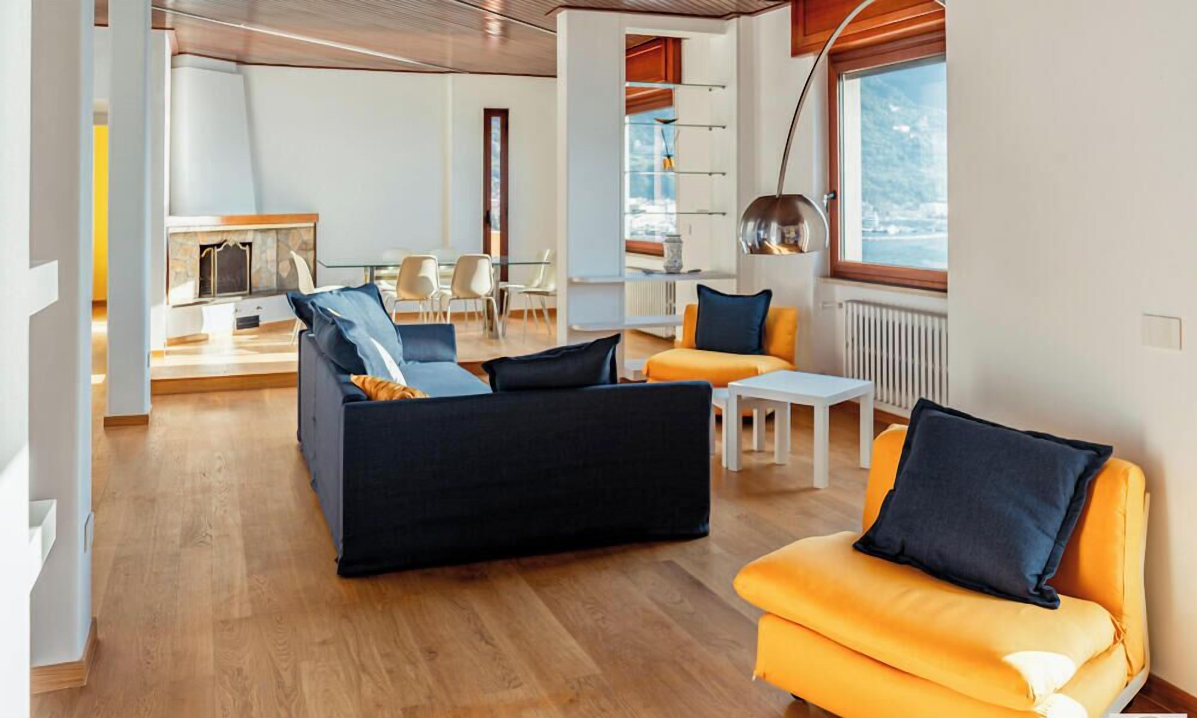 Ein modernes Wohnzimmer mit Sofa, Sessel und Couchtisch. Im Hintergrund ist eine Essecke mit Stühlen und einem Tisch zu sehen.