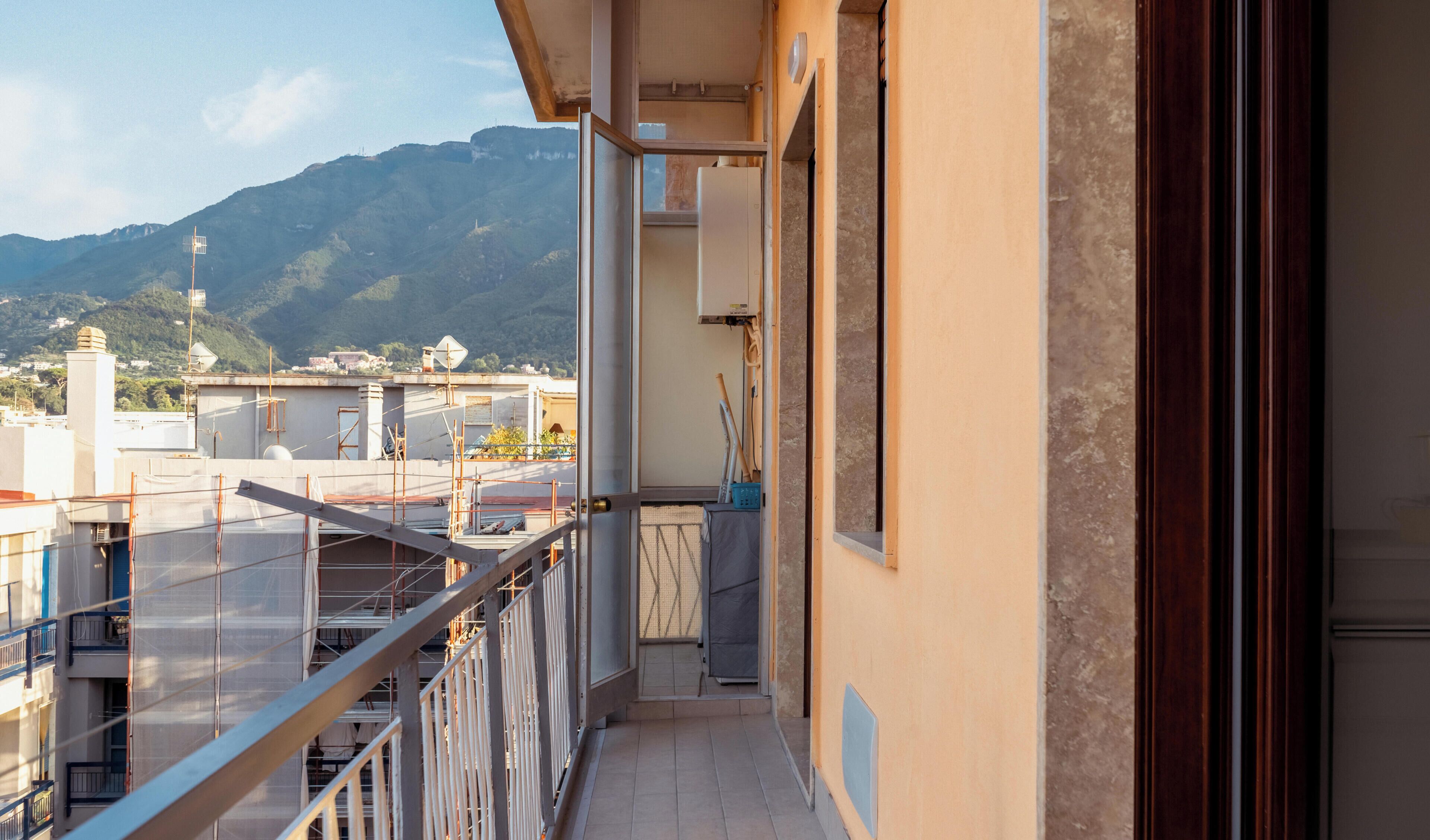 Ein Balkon mit Blick auf eine gebirgige Landschaft, ein Gebäude mit Gerüst und ein klarer Himmel.