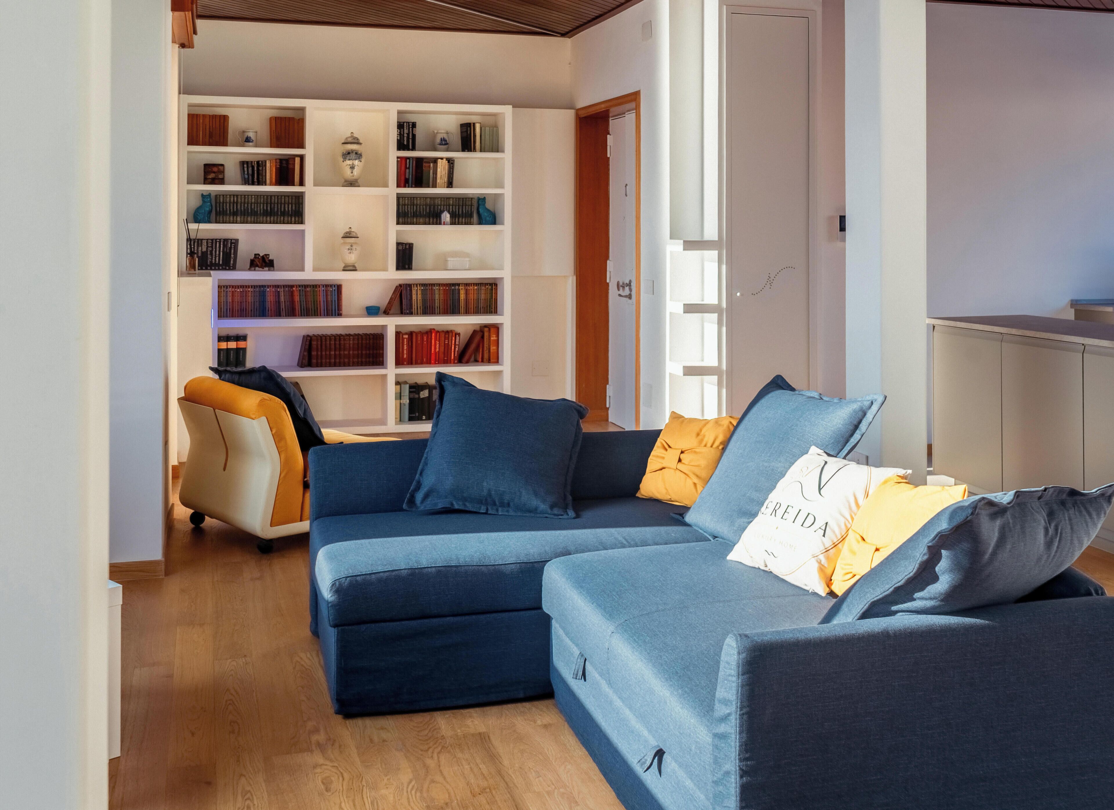 Ein modernes Wohnzimmer mit einem Ecksofa, einem Bücherregal voller Bücher und Dekoration sowie einem Holzboden.