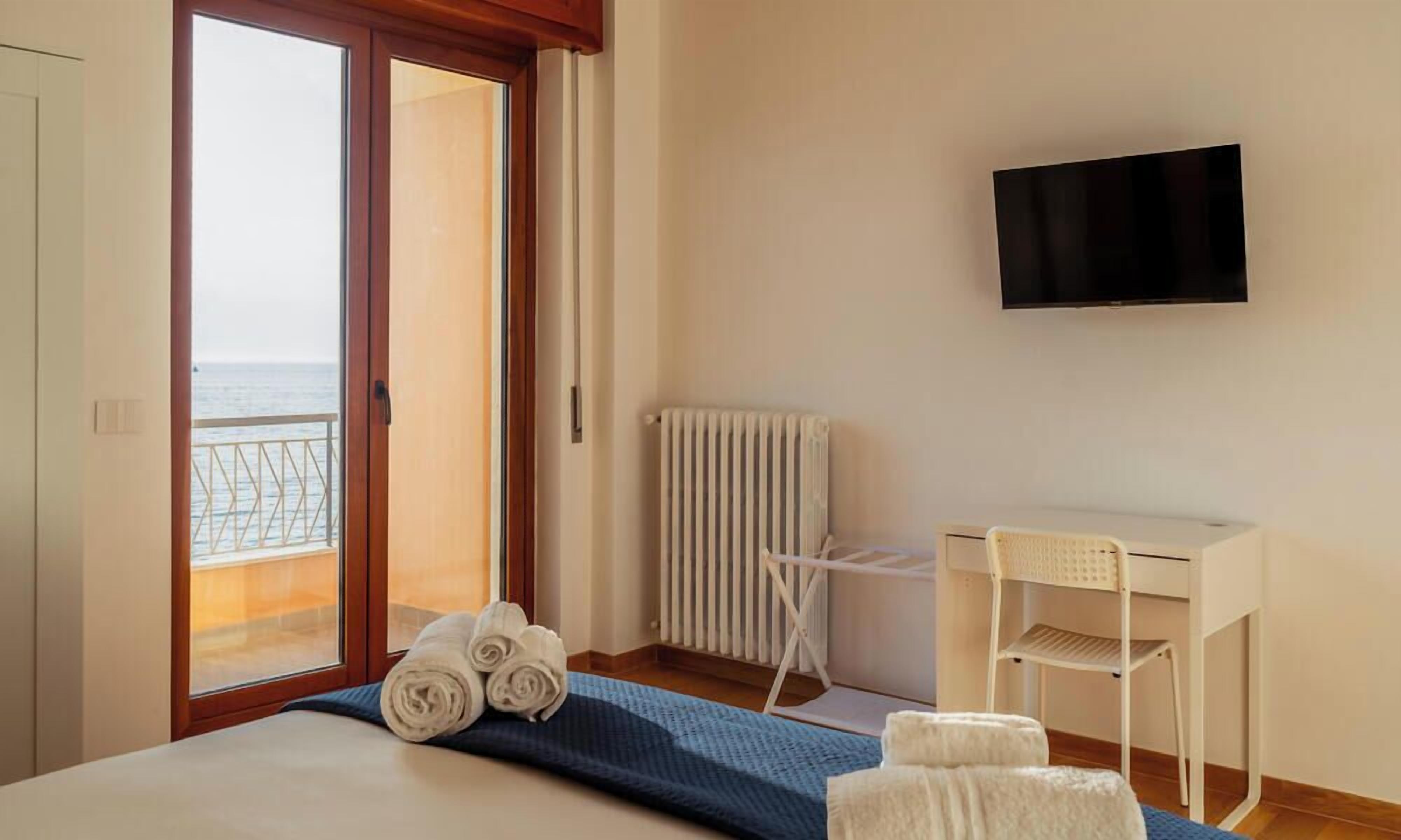 Une chambre d’hôtel équipée d’un lit, d’un bureau, d’une chaise, d’une télévision et offrant une vue sur la mer grâce à une porte coulissante.