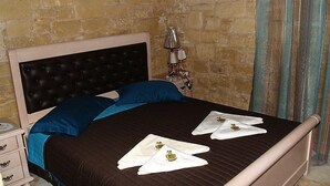 A neatly made bed with a dark headboard, blue pillows, and two white towels with a crest. - Palazzo Loupassi Boutique Hotel (Platanias)