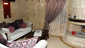 A cozy room with a stone wall, a white sofa with patterned cushions, a wooden coffee table, and a fireplace with a white mantel. - Palazzo Loupassi Boutique Hotel (Platanias)