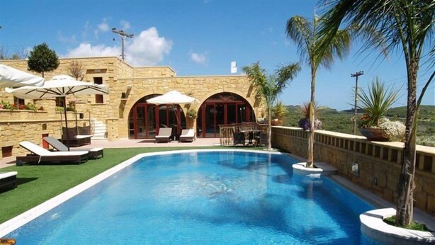 A swimming pool with lounge chairs and umbrellas, surrounded by a stone building with arched doorways. - Palazzo Loupassi Boutique Hotel (Platanias)