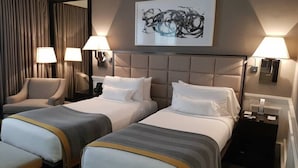 Une chambre d’hôtel avec deux lits, une chaise, une grande peinture abstraite et deux lampes de chevet.