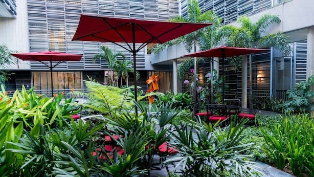 Un espace extérieur aménagé avec des parasols rouges, une végétation luxuriante et une architecture moderne.