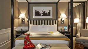 Une chambre d’hôtel avec un lit, deux tables de chevet, une petite table, une chaise, une lampe, un tableau encadré au mur et un magazine sur le lit.