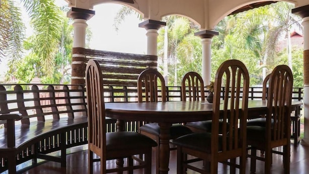 A covered outdoor seating area with a round table and chairs, surrounded by columns and a view of tropical foliage. - Sunny Days Homestay Champakkulam (Kuttanad Taluk)
