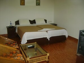 Habitación de hotel con una cama doble, una mesita de noche pequeña, una botella de agua, un control remoto, una silla de mimbre y un televisor.