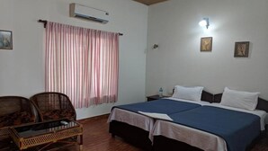 A room with a bed, two nightstands, a wall-mounted air conditioner, a window with curtains, and two wicker chairs. - Sunny Days Homestay Champakkulam (Kuttanad Taluk)