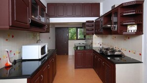 A kitchen with dark wooden cabinets, a white microwave, and a gas stove. - Sunny Days Homestay Champakkulam (Kuttanad Taluk)