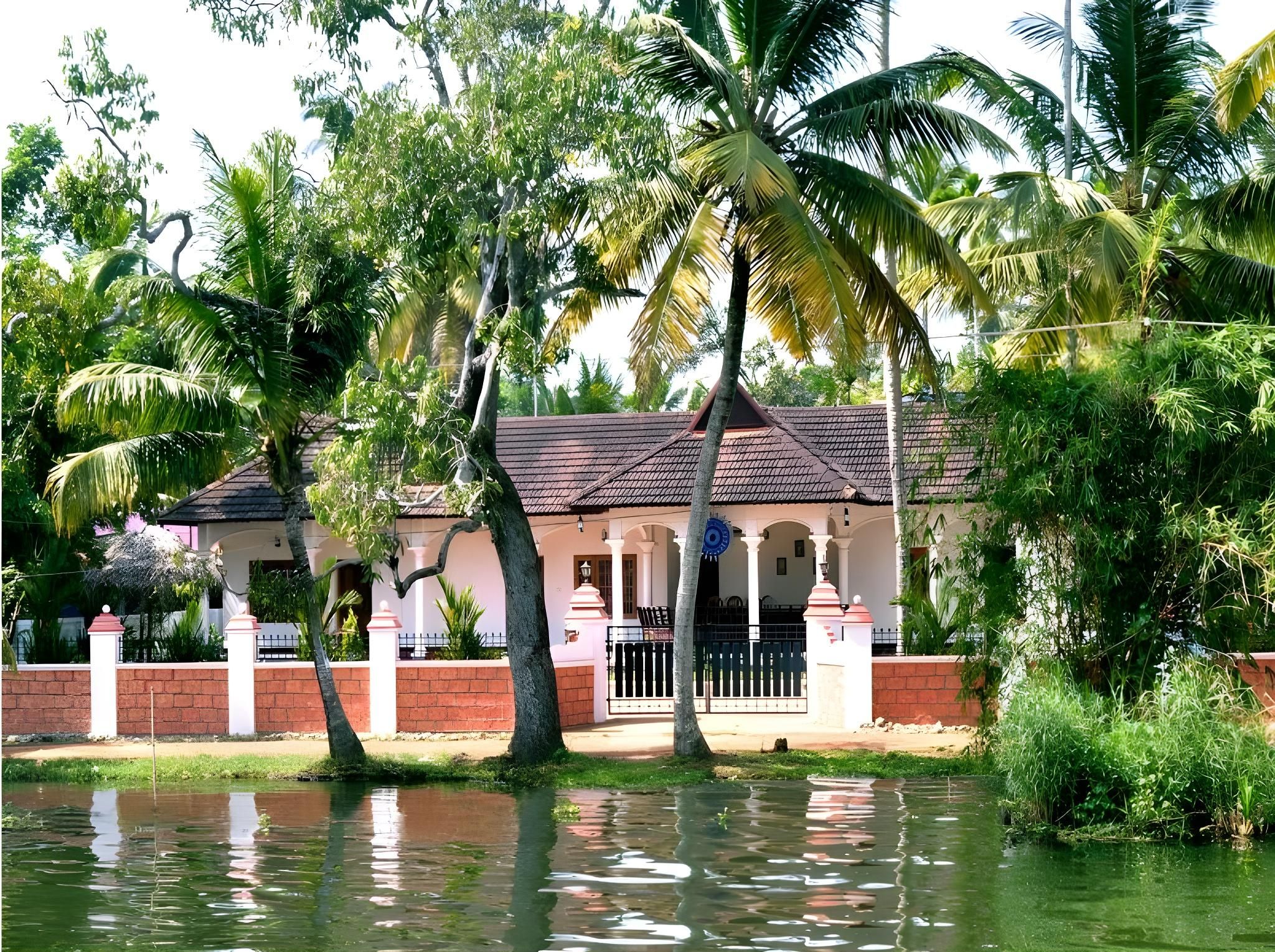 A house with a tiled roof, surrounded by palm trees and a water body.