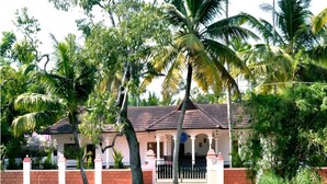 A house with a tiled roof, surrounded by palm trees and a water body. - Sunny Days Homestay Champakkulam (Kuttanad Taluk)