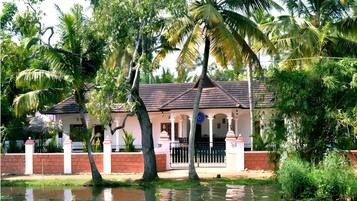 A house with a tiled roof, surrounded by palm trees and a water body.