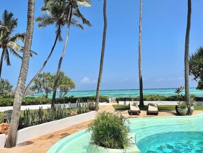 A poolside area with lounge chairs, palm trees, and a view of the ocean.