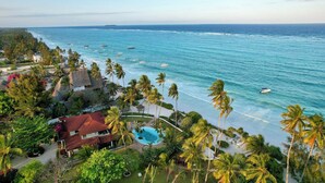 Un resort costero con piscina, acceso a la playa y palmeras.