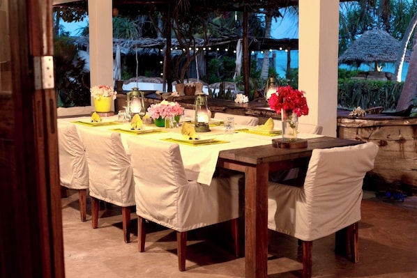 An outdoor dining area with a table set for four, surrounded by chairs, and decorated with flowers and lanterns.