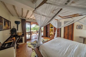A bedroom with a canopy bed, wooden furniture, a small table with a lamp, and a view of the outdoors.