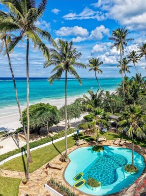 A pool area with palm trees, a beach, and a clear sky.